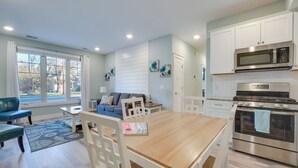 Une cuisine moderne avec des meubles blancs, des appareils en acier inoxydable et un coin repas comprenant une table et des chaises en bois.