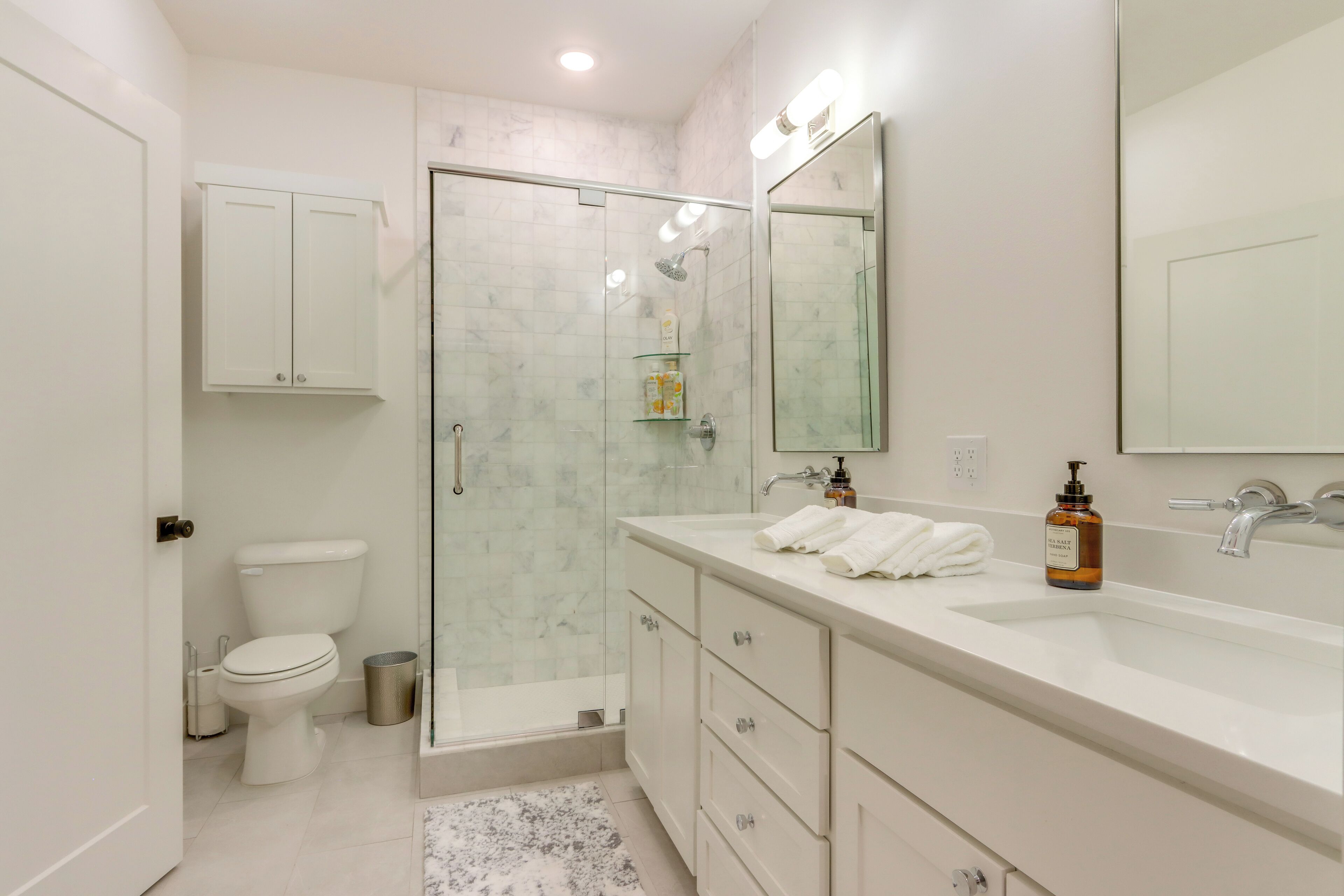 Un baño moderno con ducha de vidrio, un lavamanos blanco y un espejo grande, y un inodoro.