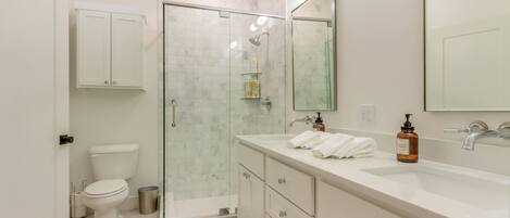 Un baño moderno con ducha de vidrio, un lavamanos blanco y un espejo grande, y un inodoro.