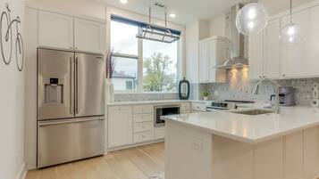 A modern kitchen with white cabinetry, stainless steel appliances, a large island with a sink, and pendant lighting.