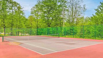 A tennis court with a net, surrounded by a green fence and trees.