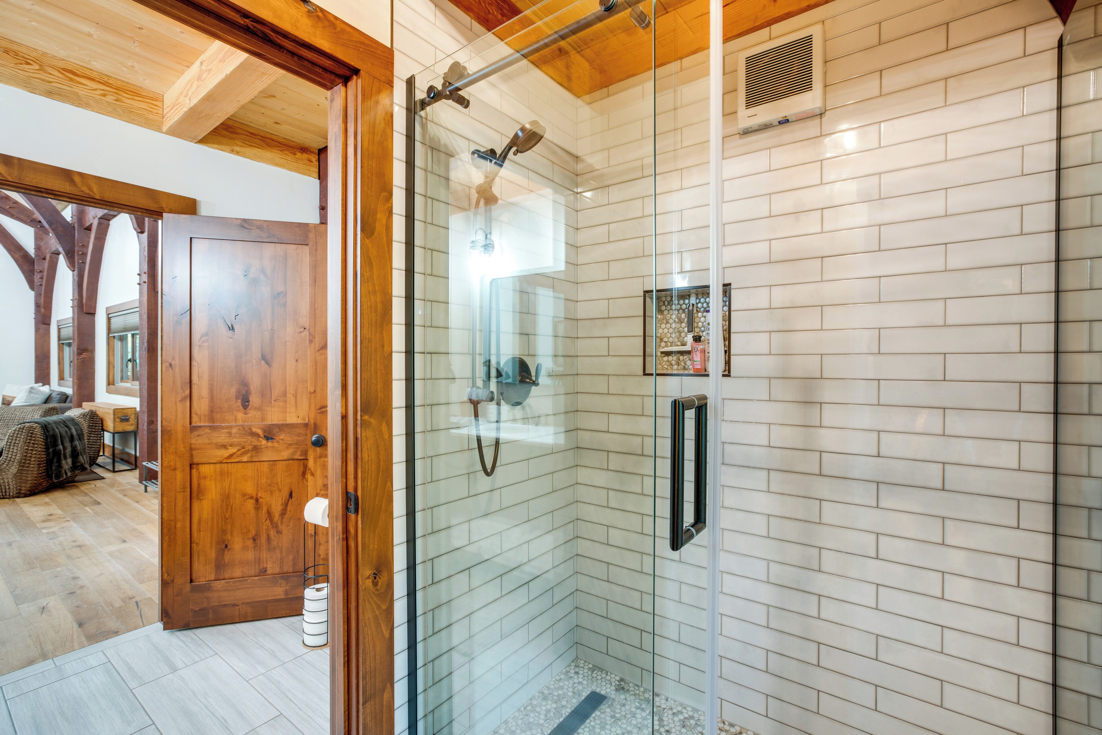 A modern bathroom with a glass shower enclosure, white tiled walls, and a wooden door.