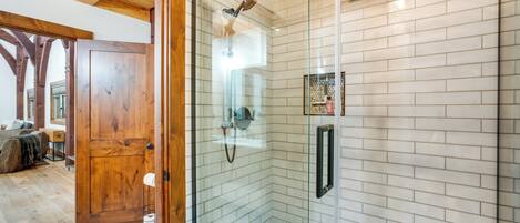 A modern bathroom with a glass shower enclosure, white tiled walls, and a wooden door.