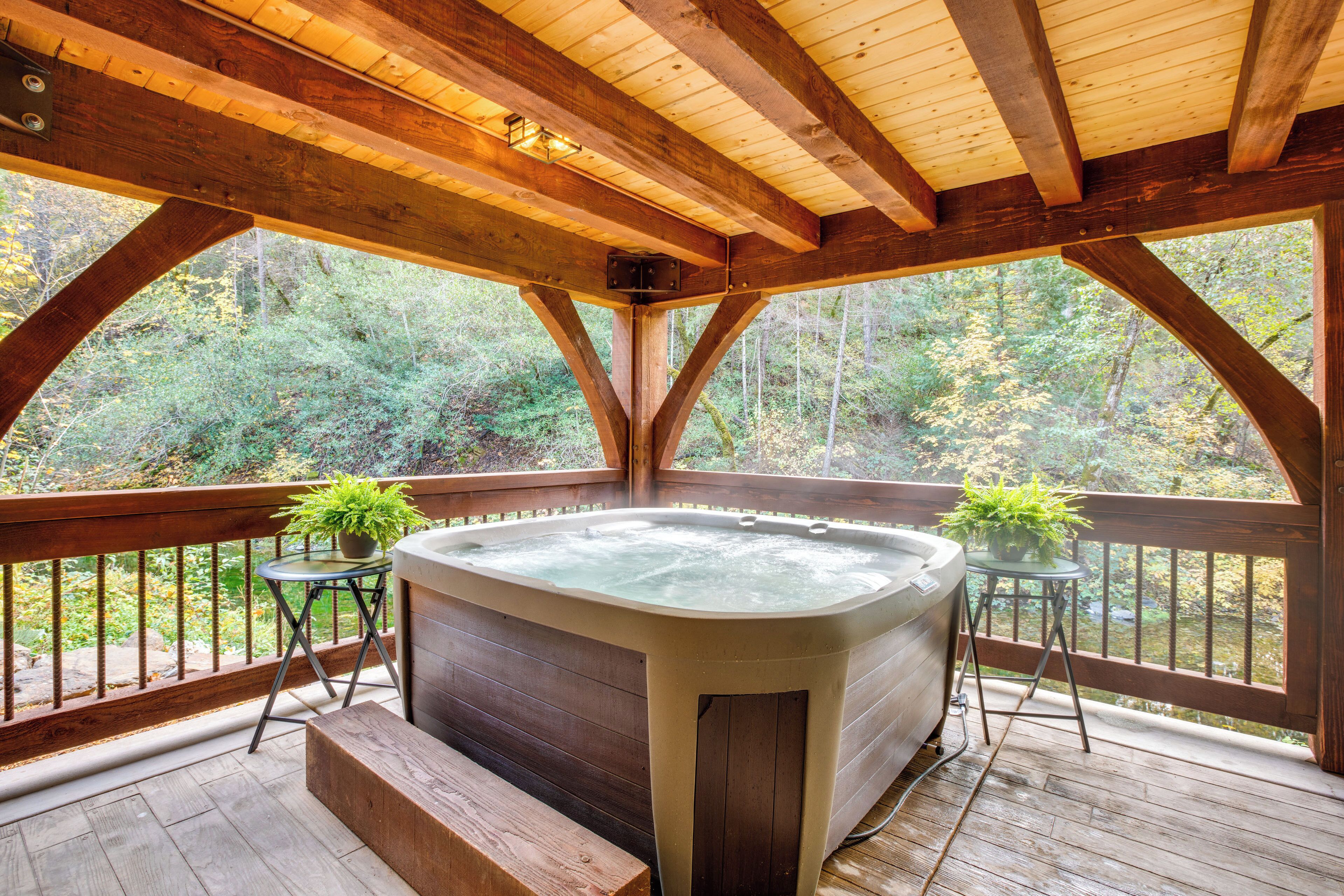 A wooden deck with a hot tub, two potted plants, and a view of a forest.