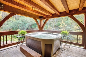 A wooden deck with a hot tub, two potted plants, and a view of a forest.