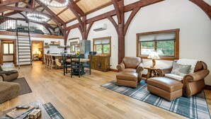 A spacious living area with wooden beams, leather furniture, and a dining area with a view of the outdoors. - Bear Lodge Waterfront Cabin w/ Level 2 EV Charger (Sutter Creek)