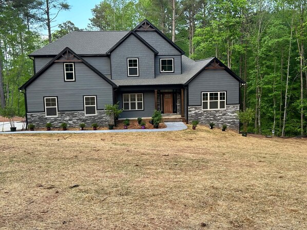 A two-story house with a stone foundation, multiple windows, and a front porch. - Whispering Winds | Brand New Lakefront 6BR on Lake Norman | Sleeps 15 | Free Pedal Boat (Catawba)