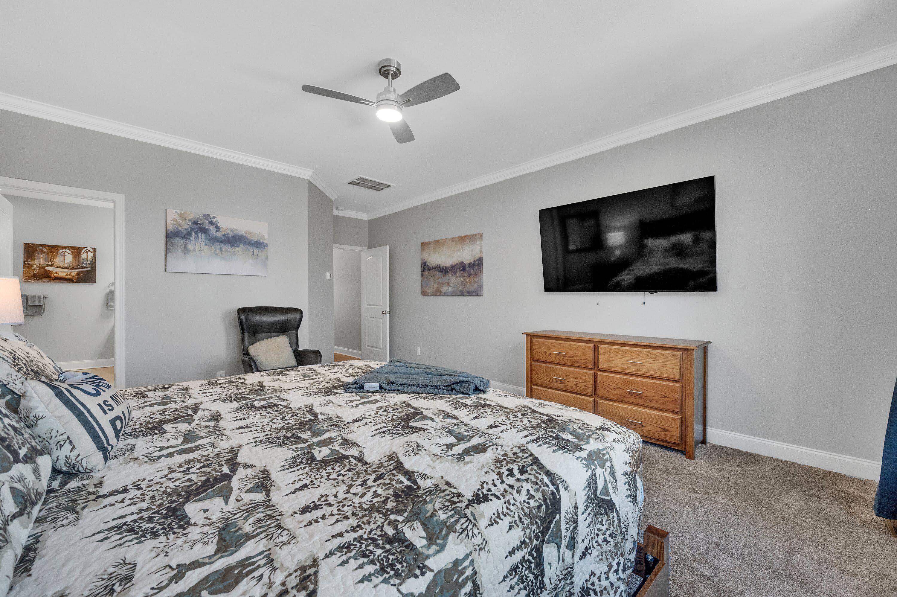 Une chambre à coucher avec un lit, un ventilateur de plafond, une commode et des œuvres d’art accrochées aux murs.