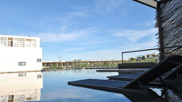 A rooftop pool with lounge chairs, a clear sky, and a modern building in the background. - New Chic Tulum with Rooftop Pool (Tulum)