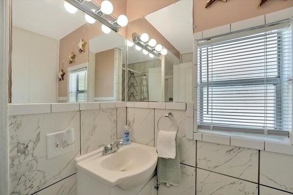 Ein Badezimmer mit Waschtisch, Spüle, einem Spiegel mit Beleuchtung und einem Fenster mit Jalousien.