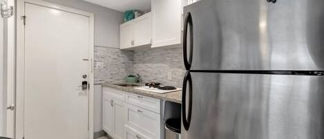 A compact kitchen with white cabinets, a stainless steel refrigerator, and a tiled floor.