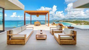 A modern outdoor seating area with wooden furniture and a view of the ocean. - Villa Amandara – Iconic Luxury Estate in St. Martin (Les Terres Basses)