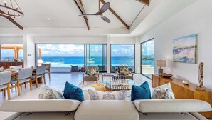 A spacious living area with a large window overlooking the ocean, a dining area, and a view of the sea. - Villa Amandara – Iconic Luxury Estate in St. Martin (Les Terres Basses)