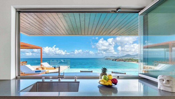 A kitchen with a large window overlooking a pool and ocean view. - Villa Amandara – Iconic Luxury Estate in St. Martin (Les Terres Basses)