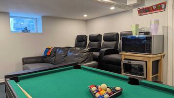 A pool table with balls, a sofa with a blanket, a microwave, and a snack bar sign.