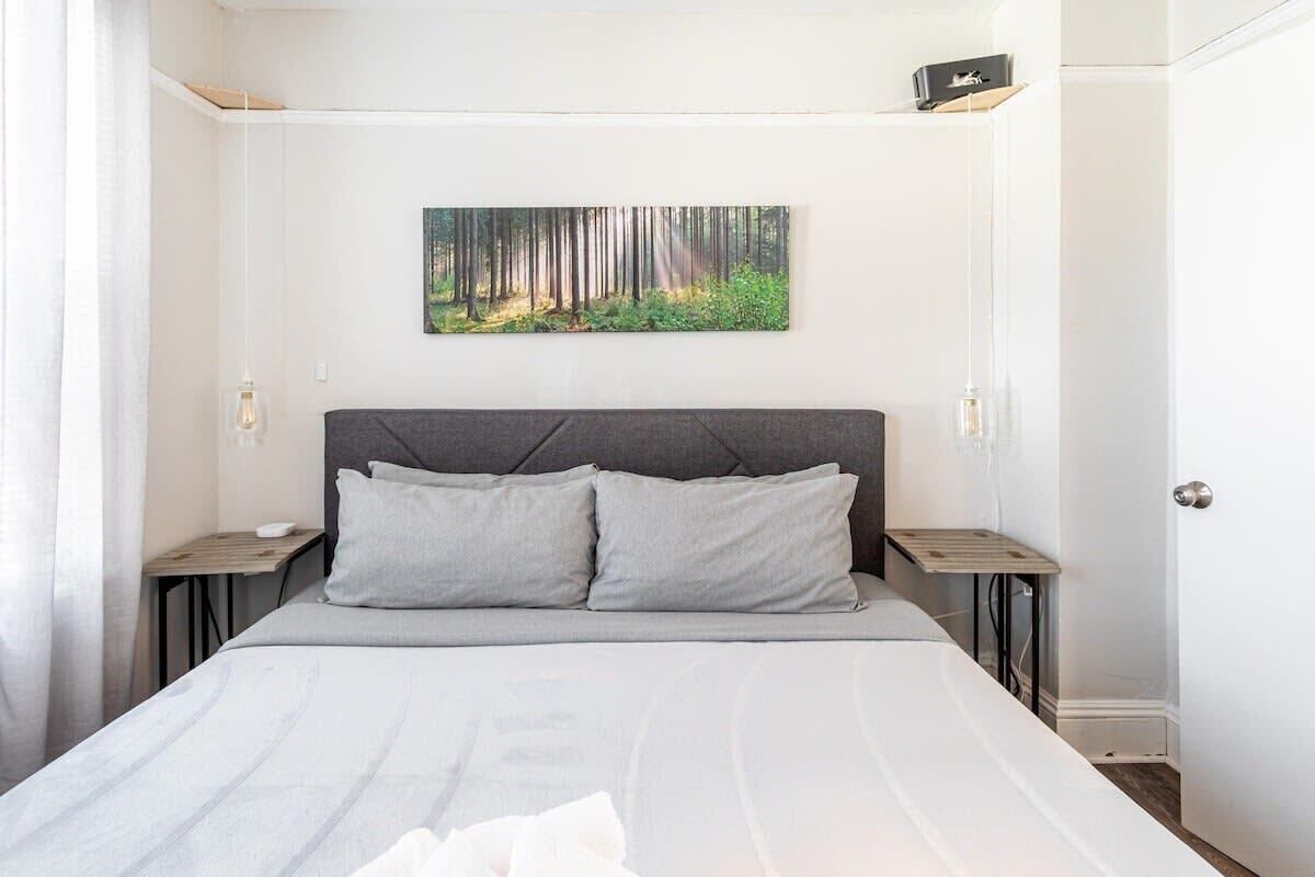 A bedroom with a bed, two bedside tables, a headboard, a wall-mounted painting, and a door.