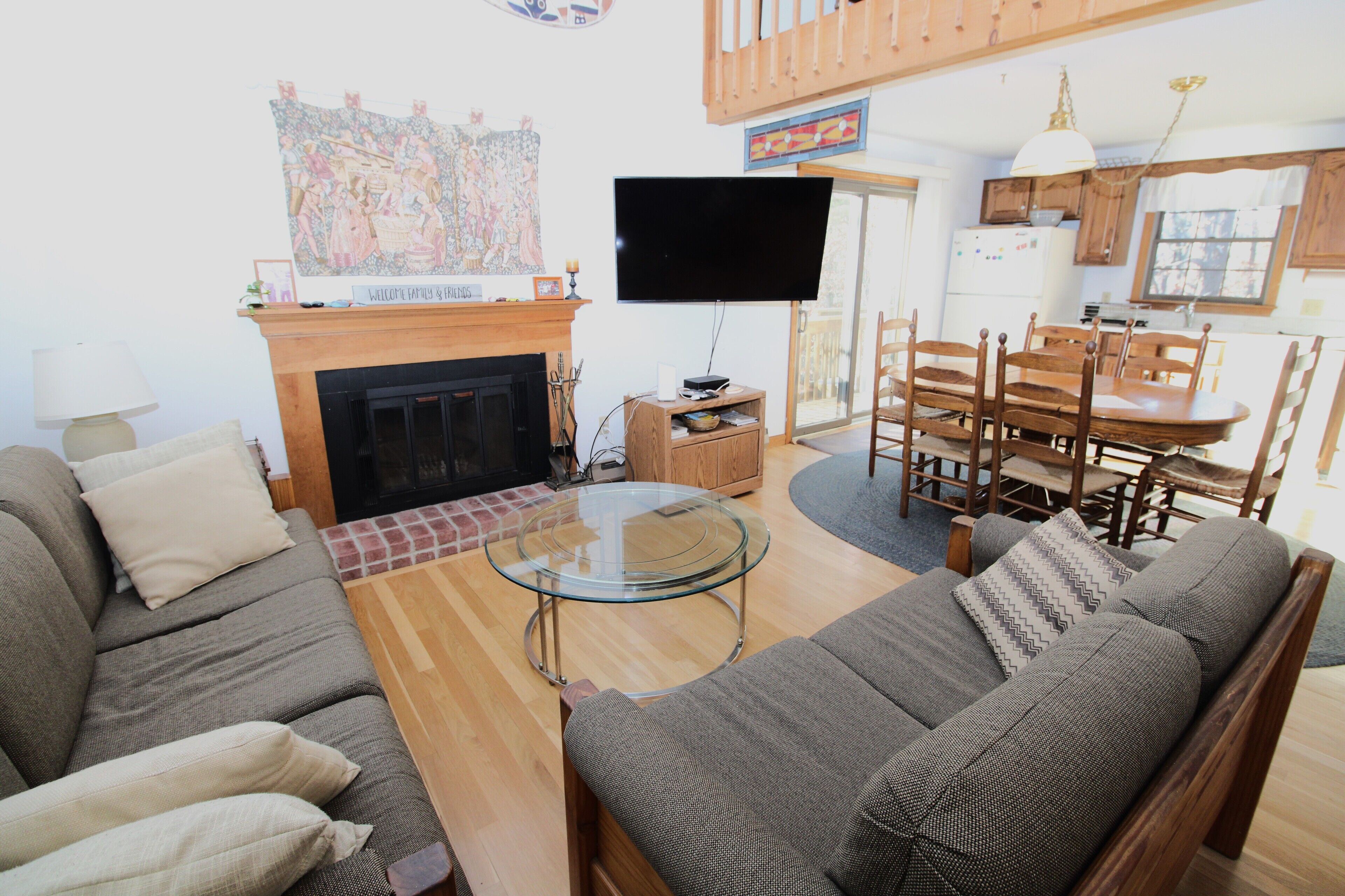A living room with a sofa, a glass coffee table, a fireplace, a TV, and a dining area with a wooden table and chairs.