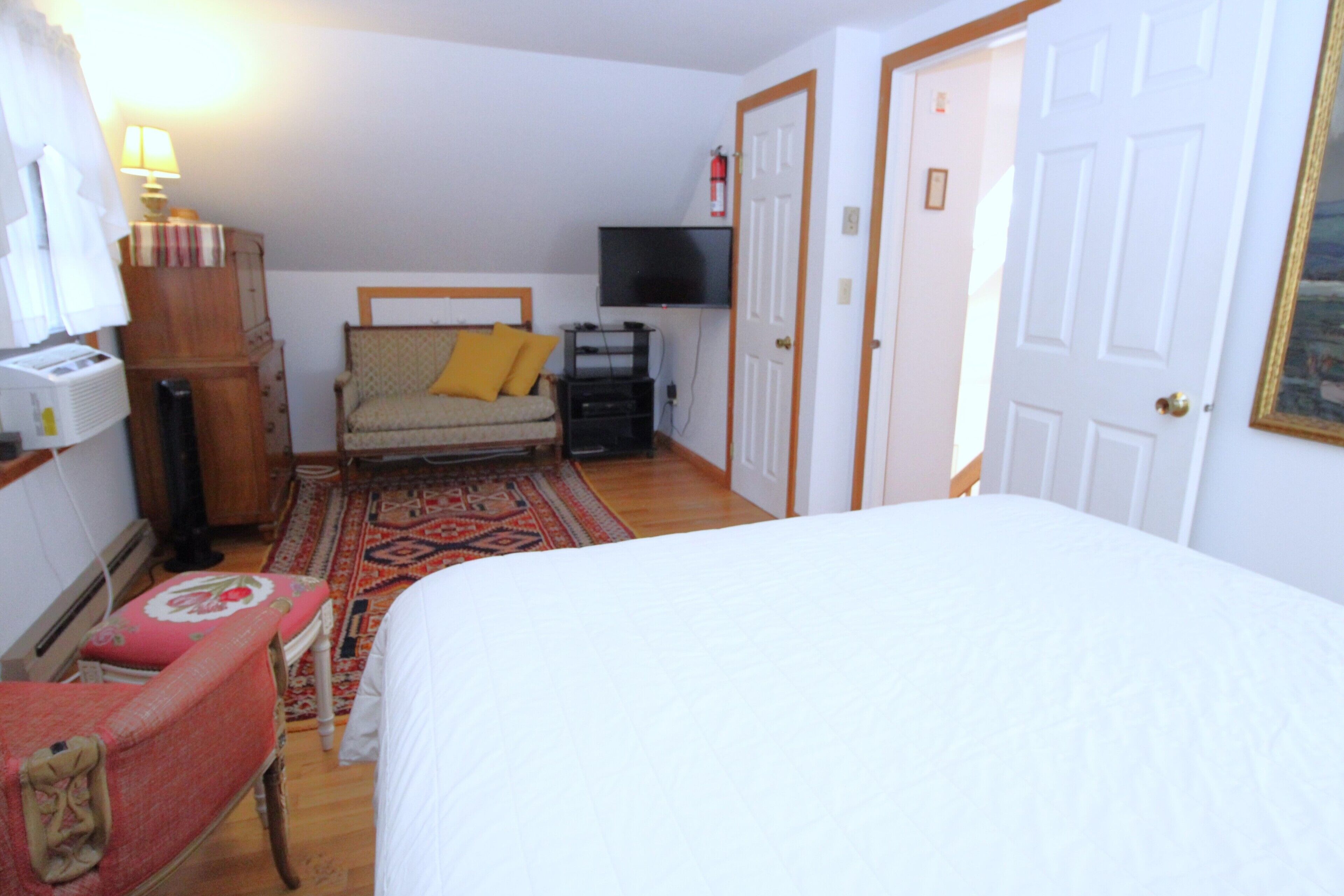 Ein Schlafzimmer mit Bett, Sessel, Fernseher und Kleiderschrank.