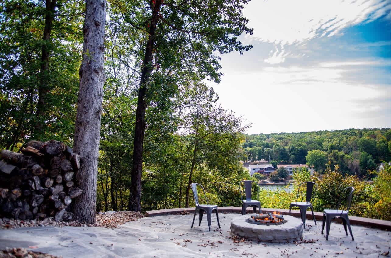Un espace extérieur aménagé avec des chaises et un foyer, entouré d’arbres et offrant une vue panoramique.