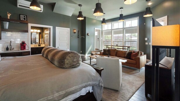 A bedroom with a large bed, a sofa, and a coffee table. There are pendant lights and a window with a view. - Rackensack Inn Summar (Bentonville)