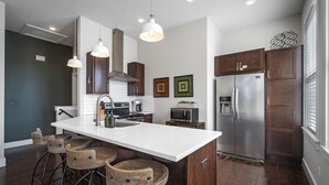 A modern kitchen with a central island, stainless steel appliances, and wooden bar stools. - Rackensack Inn Summar (Bentonville)