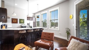 A modern kitchen with a bar area, wooden flooring, and large windows. - Rackensack Inn Summar (Bentonville)