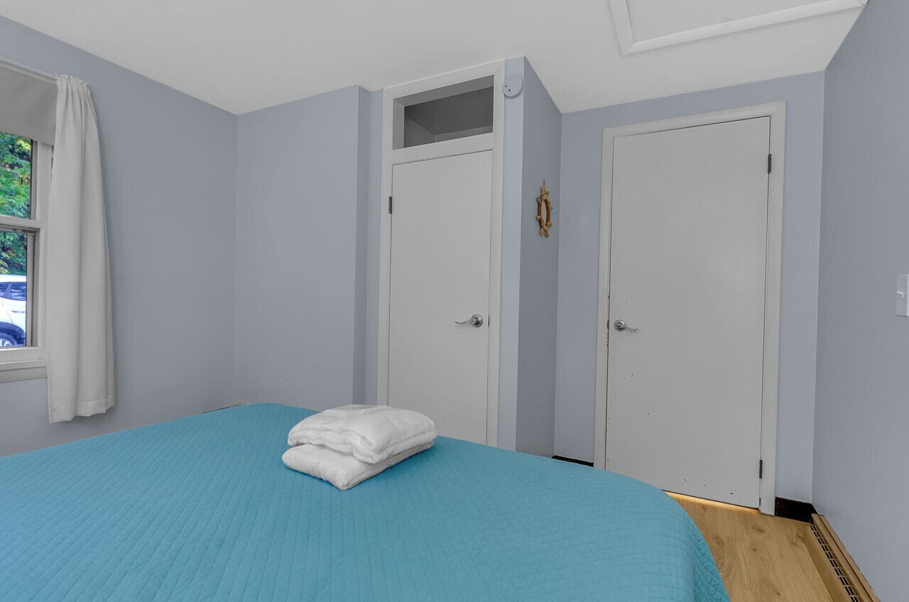 A bedroom with a bed, a window with curtains, and two doors.