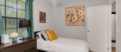 Quarto com cama, penteadeira, luminária e obra de arte na parede.