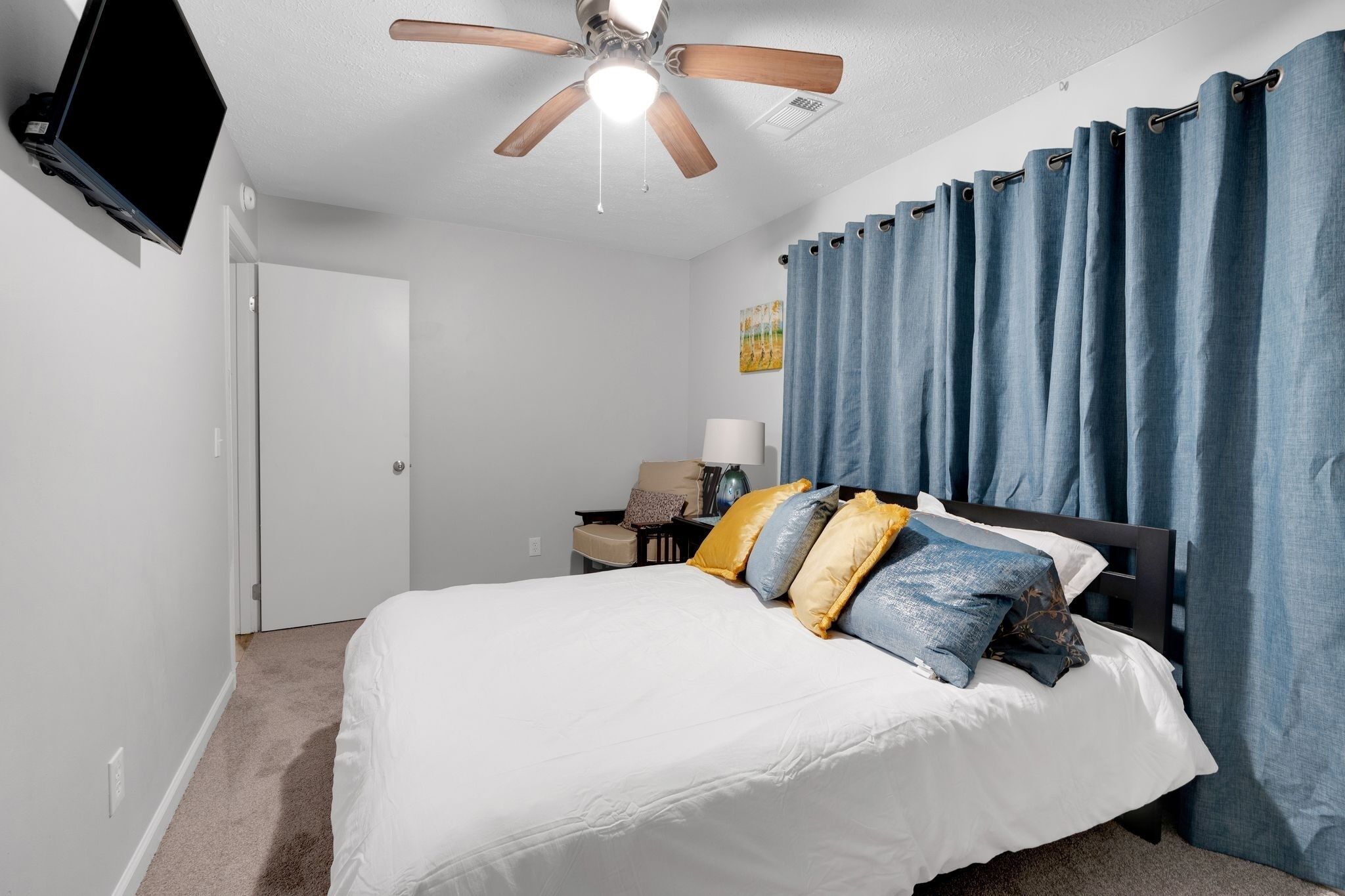 A bedroom with a bed, a ceiling fan, a TV, a nightstand, and a door.