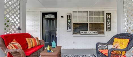 A porch with wicker furniture, a red sofa, a wicker chair, and a patterned rug.