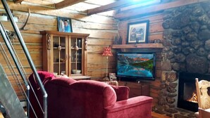 Interior acogedor de una cabaña de madera con un sofá rojo, televisor, chimenea y una pared de piedra.