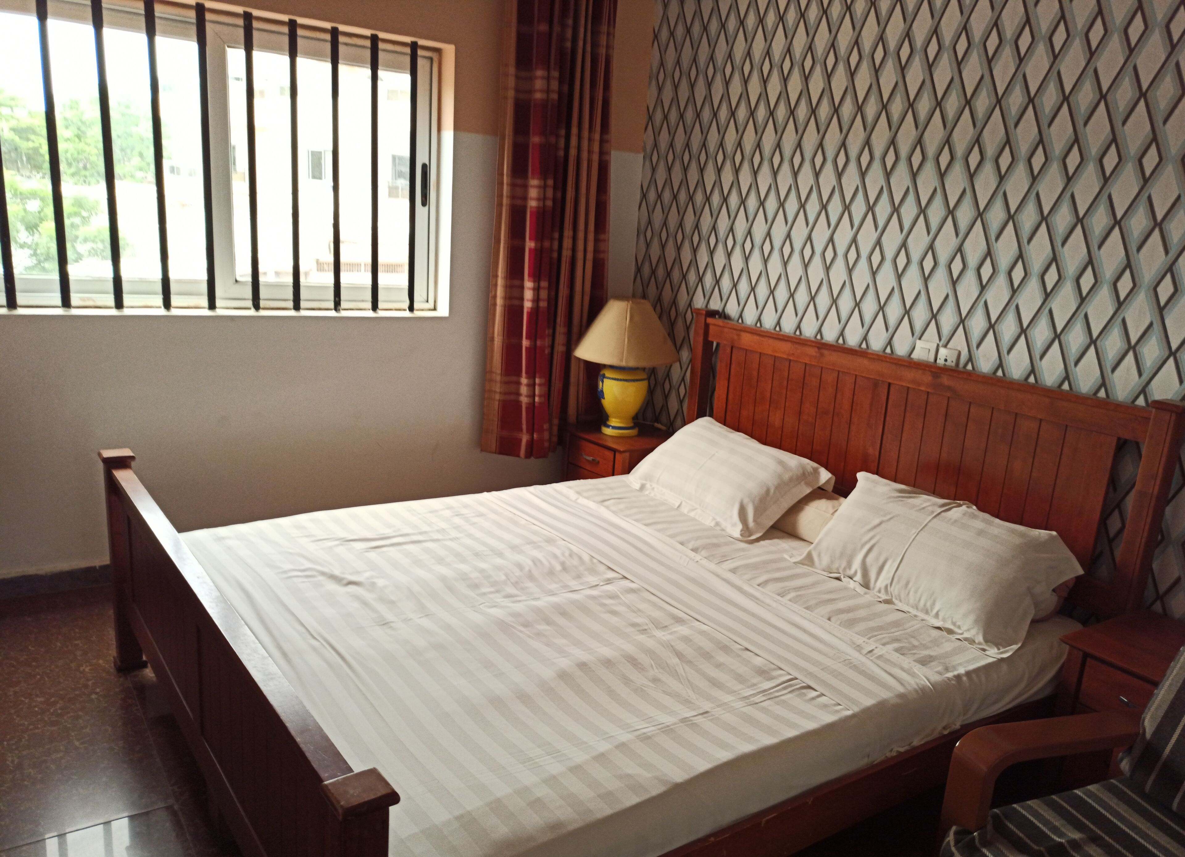 A neatly made bed with a wooden headboard and a patterned wall behind it.