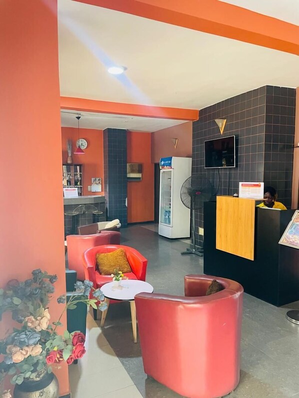 A reception area with a counter, a fan, and seating arrangements. - HOTEL ST JEAN (Cotonou)