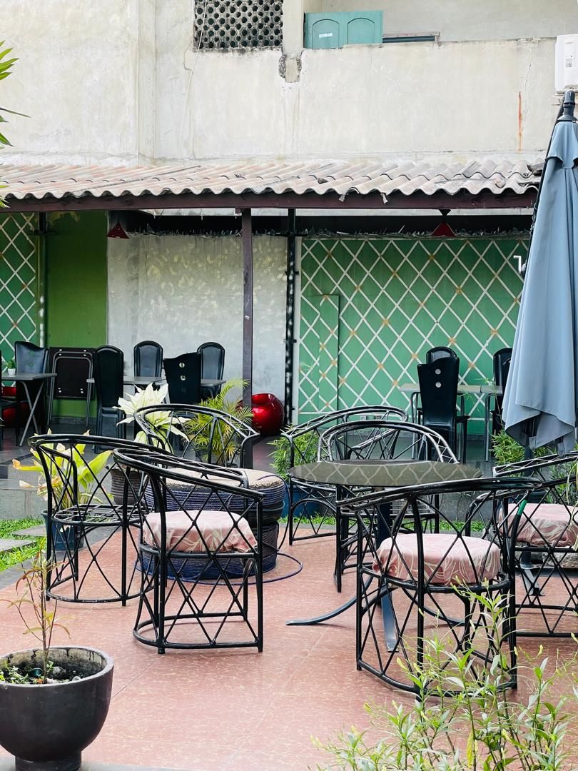 An outdoor patio area with metal chairs and tables, a potted plant, and a green wall in the background.