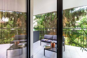 A balcony with a sofa, a glass table, and a potted plant.
