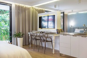 Une chambre d’hôtel moderne équipée d’un lit, d’un bureau avec des chaises, d’une télévision, d’un balcon avec des rideaux et d’un lavabo.