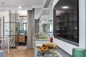 A modern kitchen with a large window, a chandelier, and a dining area with transparent chairs.