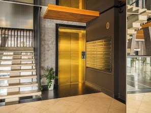 Un elevador moderno con acabados metálicos, una planta en maceta y un buzón instalado en la pared.
