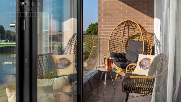 A balcony with wicker chairs, a table with a drink, and a view of a river.