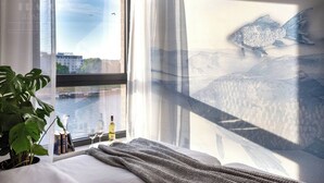 A hotel room with a large window, a bed, a plant, and a view of a river and buildings.