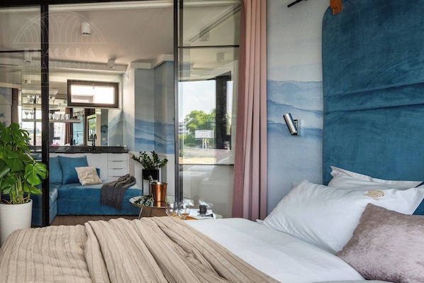 Un dormitorio moderno con una cama grande, un sofá azul, un separador de vidrio y vistas al exterior.