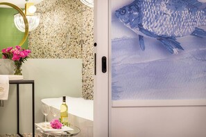A bathroom with a mosaic tile wall, a mirror, a sink with a towel, a vase with flowers, and a wine bottle on a tray. - Apartment Vistula 3-bed with a balcony and bathtub (Kraków - Vistula View)