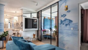 A modern living room with a blue sofa, a flat-screen TV, and a dining area with a table and chairs.
