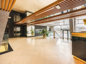 Un vestíbulo espacioso con diseño moderno, que presenta un techo de listones de madera, ventanas amplias y plantas en macetas.