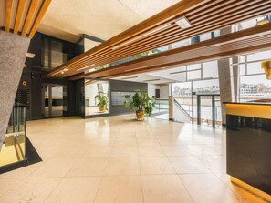 Een ruime lobby met een modern design, met een houten lattenplafond, grote ramen en potplanten.