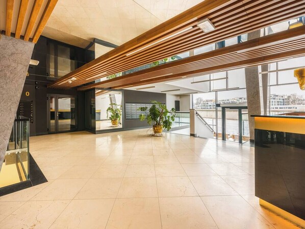 Eine geräumige Lobby mit modernem Design, inklusive einer Holzschubladen-Decke, großen Fenstern und Zimmerpflanzen.