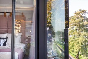 Ein modernes Schlafzimmer mit großem Fenster, einem Bett und einem Nachttisch mit Pflanze.