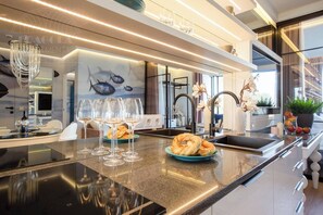Een moderne keuken met een marmeren aanrecht, wijnglazen, een bord bagels en een muurschildering van vissen op de muur.