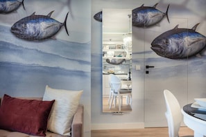 A room with a wall mural of fish, a sofa, a dining area, and a kitchen visible through an open door.