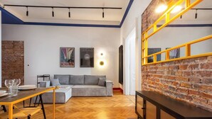 A modern living room with a herringbone wood floor, a grey sofa, a yellow-framed mirror, and a brick accent wall. - The Geometric 3-bedroom apartment (Kraków – Old Town)